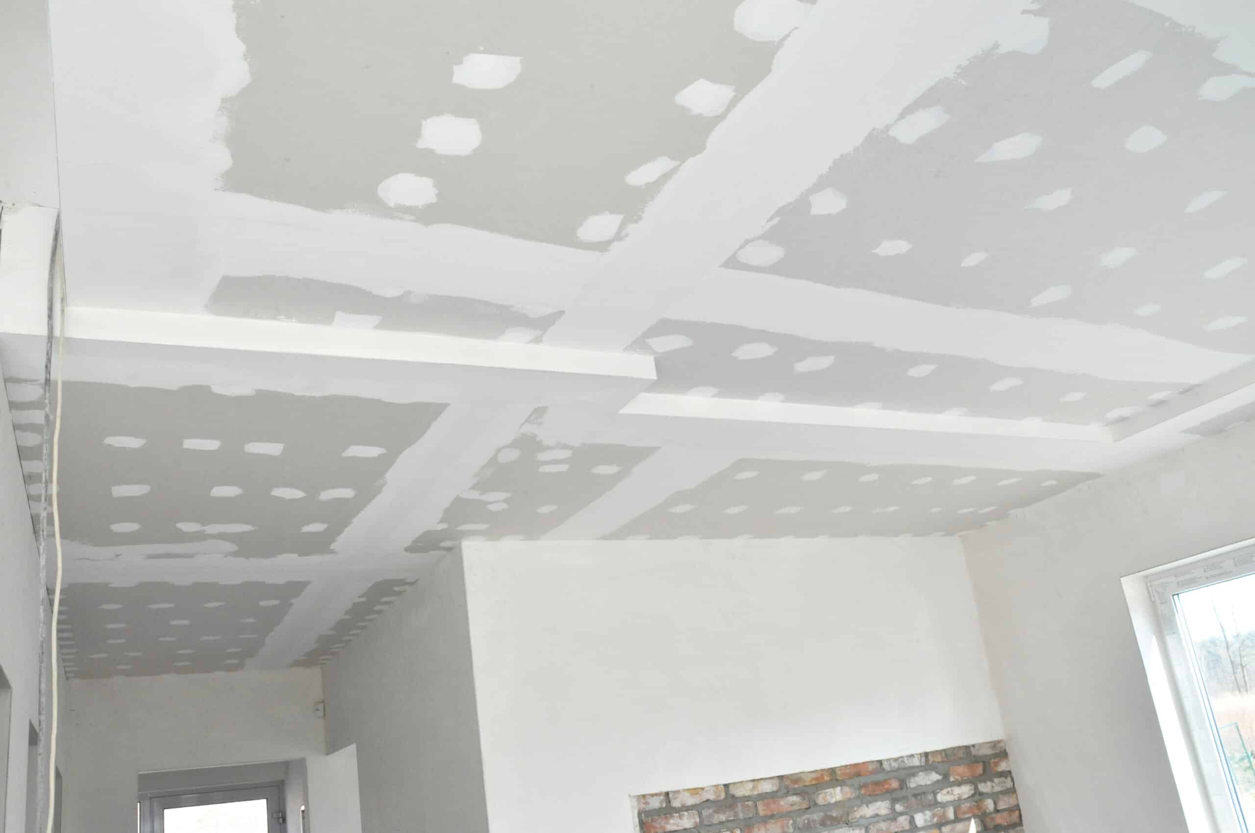 Plafond en plaques de plâtre (placo) en cours de finition avec enduit blanc, dans une pièce en rénovation. Faux plafond décoratif et mur en briques apparentes.
