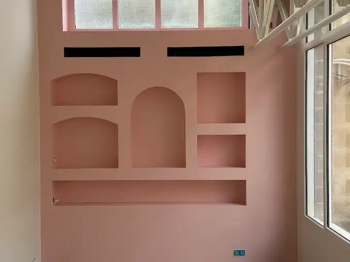 Mur Rose avec Niches Intégrées : Design Intérieur Moderne Mur rose moderne avec niches encastrées de formes variées, étagères murales décoratives et fenêtres en hauteur.